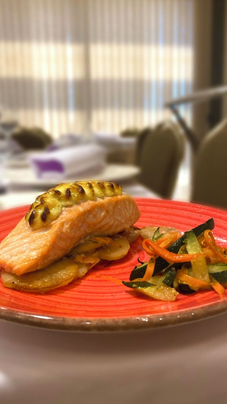 A plate with grilled salmon and vegetables on a red plate.