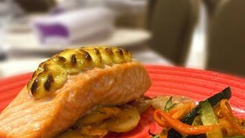 A plate with grilled salmon and vegetables on a red plate.