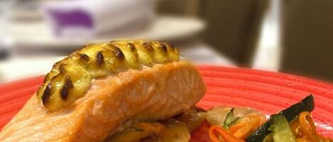 A plate with grilled salmon and vegetables on a red plate.
