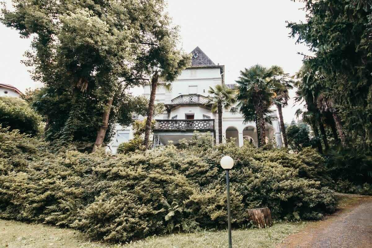 A building with a white facade and a dark roof, surrounded by dense greenery and trees.