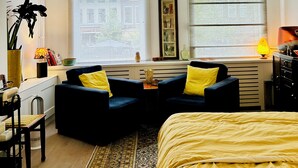 A modern bedroom with a bed, two armchairs, a small table, and a window with blinds. - Leiden City Centre Canal View Apartment in a 1750's building (Leiden)