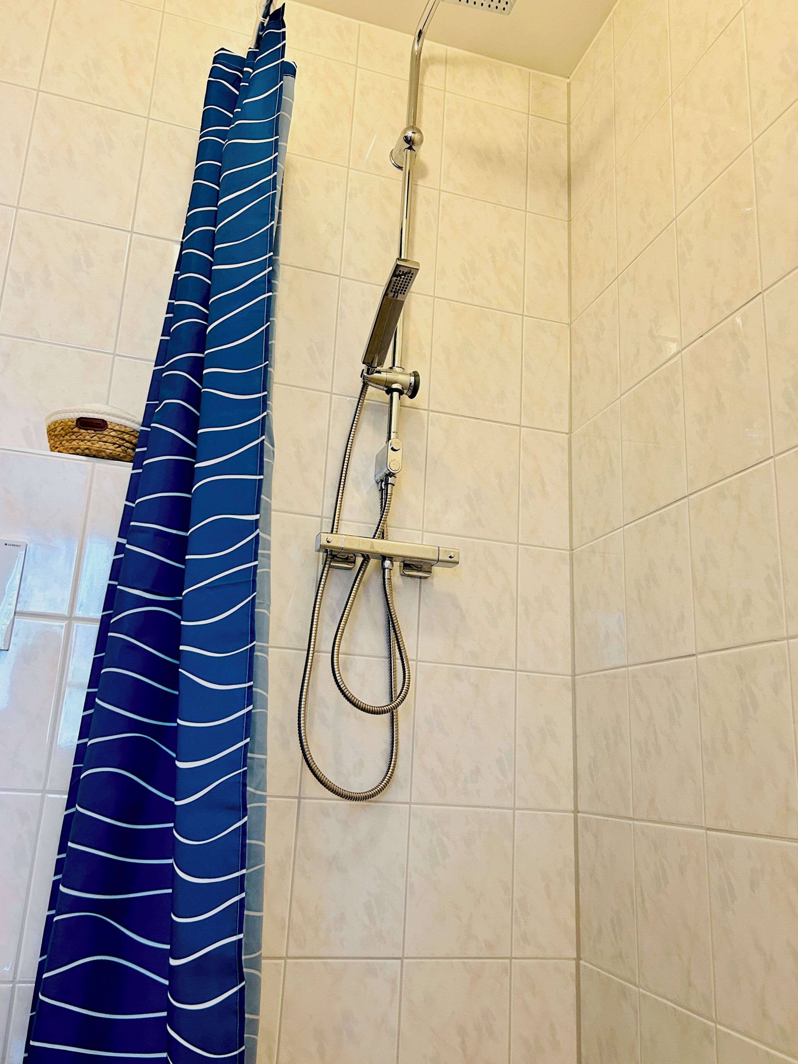 A shower with a handheld showerhead and a curtain.