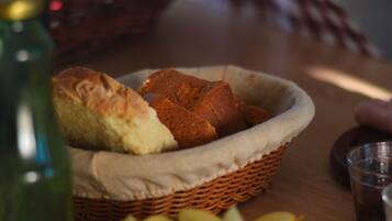 A wicker basket containing bread and a bottle on a wooden table.