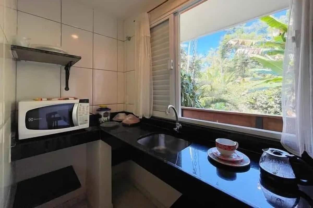 A compact kitchen with a microwave, sink, and window overlooking a lush garden.