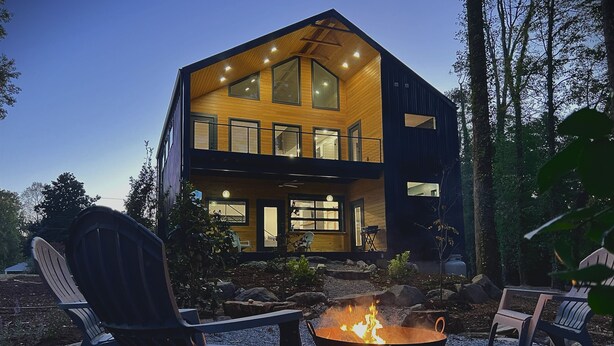 A modern two-story house with a fire pit in the front yard.