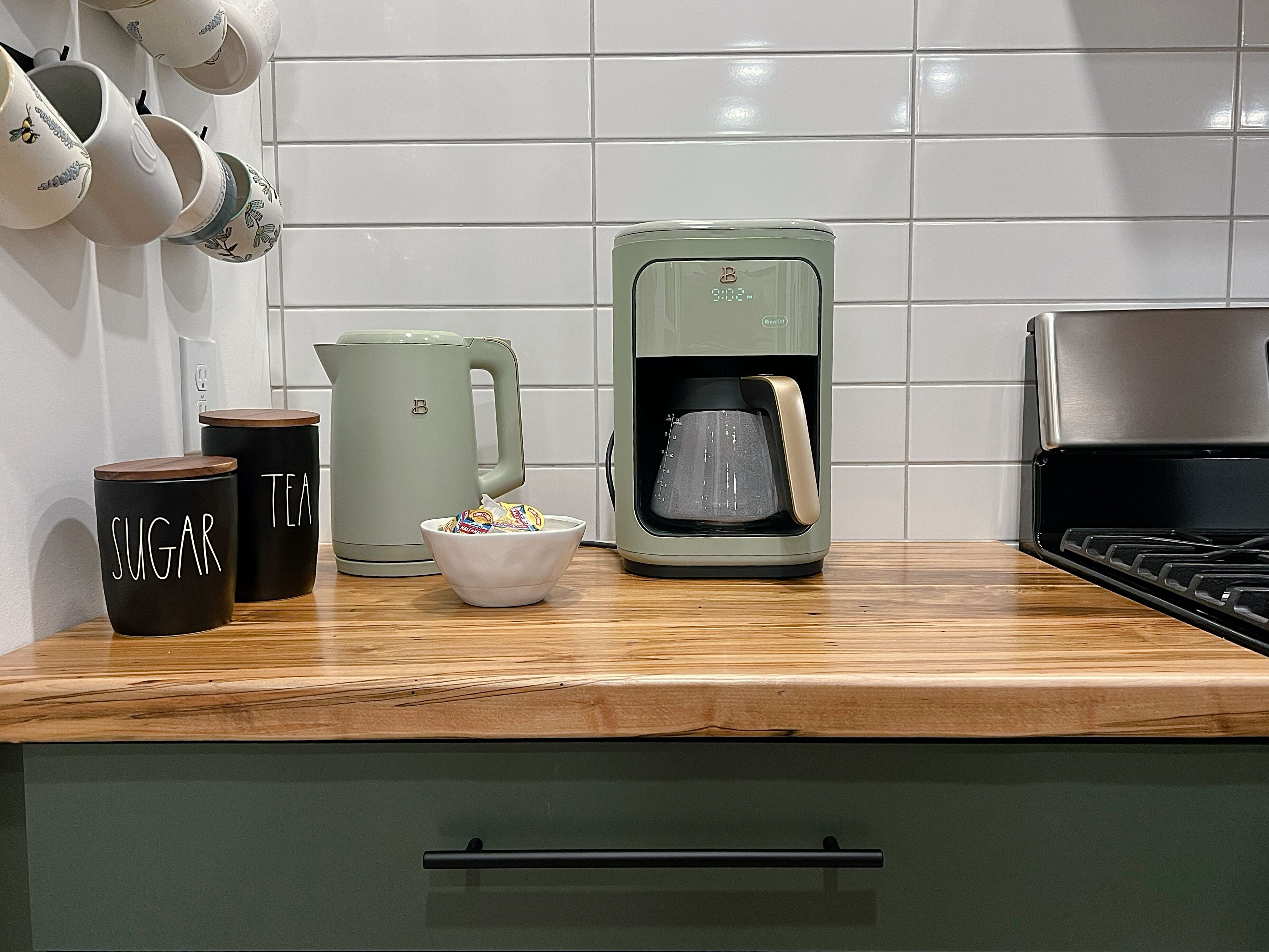 Una cocina con cafetera, azúcar y té, además de una tetera.