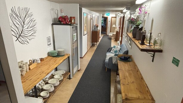 Un pasillo estrecho con un banco de madera, un refrigerador y una mesa de comedor con platos y tazones.