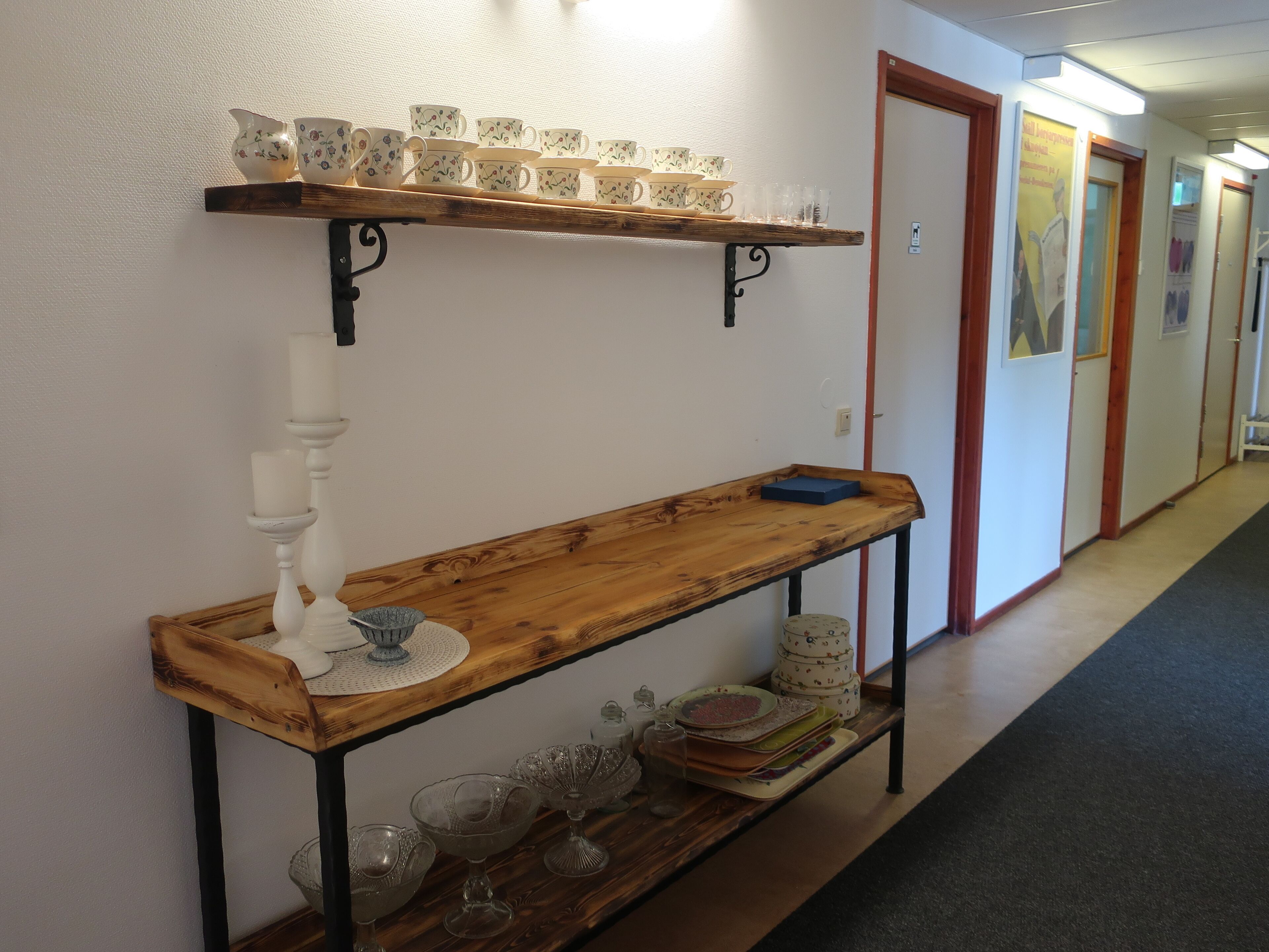 A hallway with a wooden bench, a shelf with cups and saucers, and a wall-mounted candle holder.