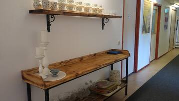 A hallway with a wooden bench, a shelf with cups and saucers, and a wall-mounted candle holder.