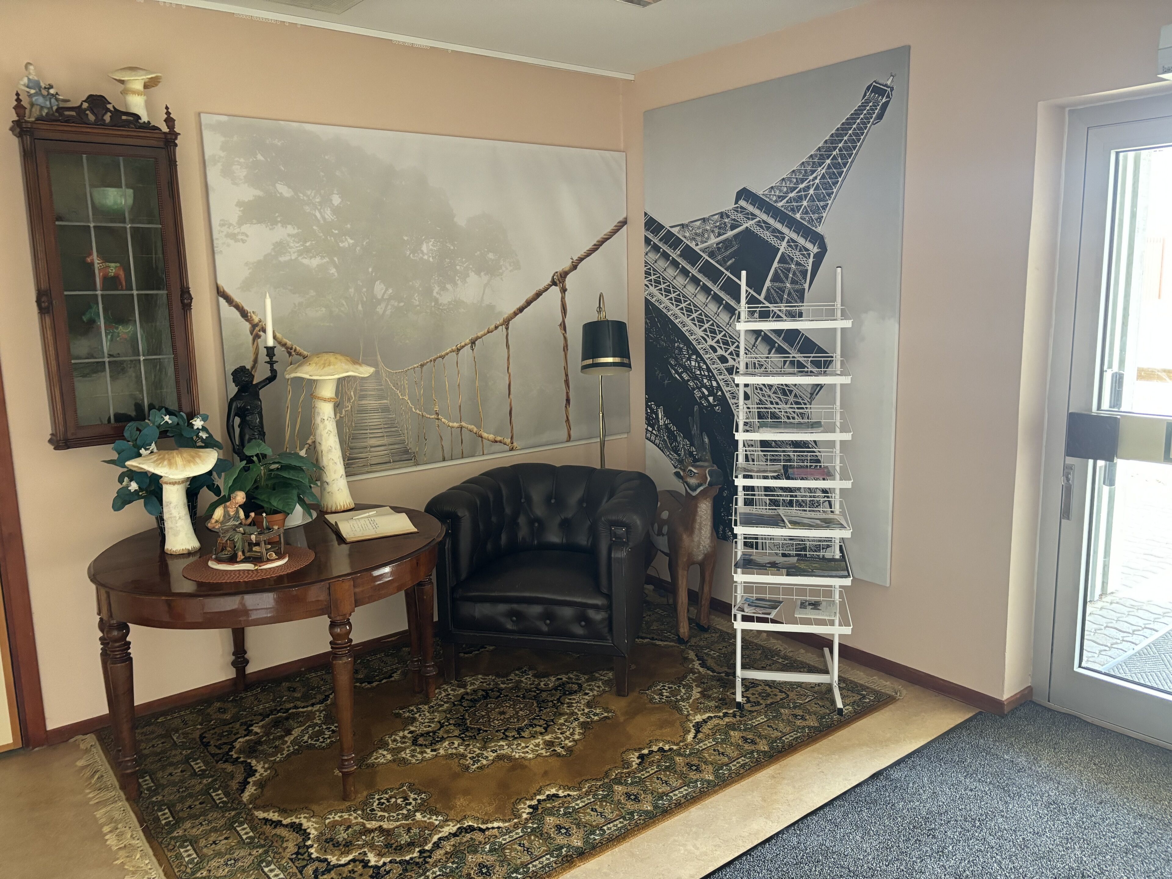 A room with a large painting of the Eiffel Tower, a black leather armchair, a wooden table with decorative items, and a white metal shelf.