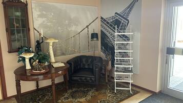 A room with a large painting of the Eiffel Tower, a black leather armchair, a wooden table with decorative items, and a white metal shelf.