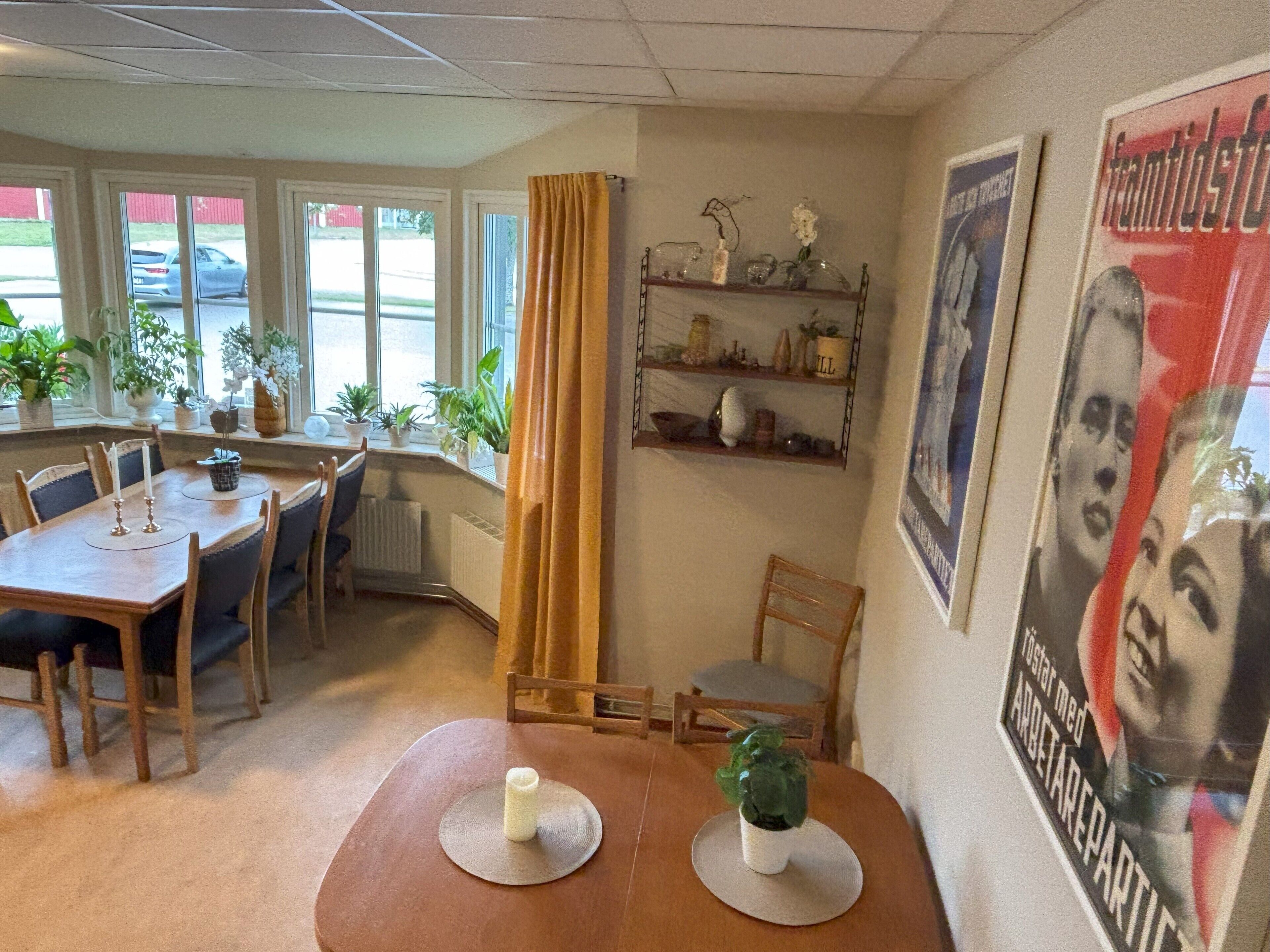 A dining area with a wooden table, chairs, potted plants, and a poster on the wall.