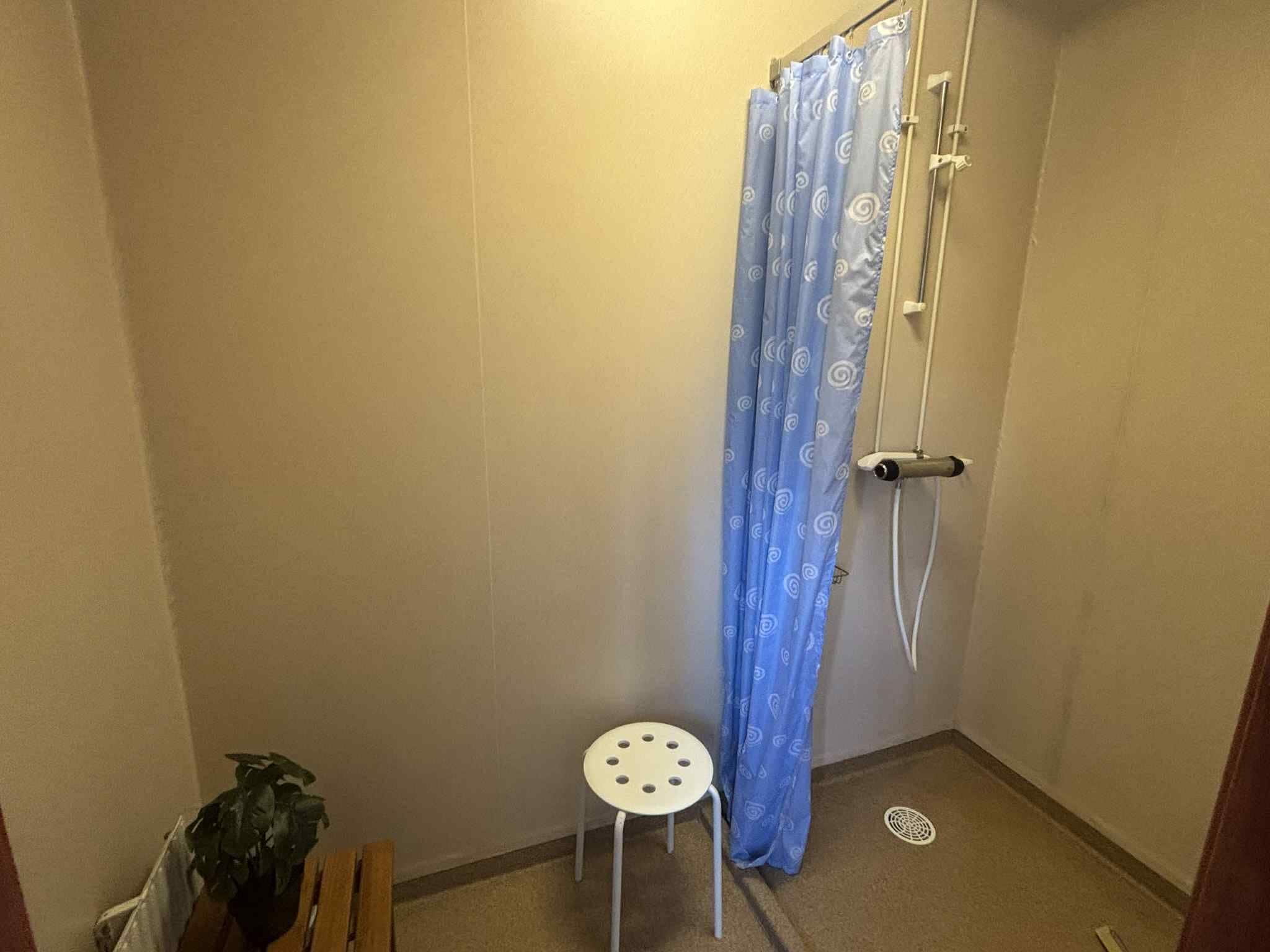 A small bathroom with a shower curtain, a white stool, and a potted plant.