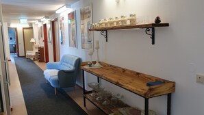Un pasillo con un sillón azul, una mesa de madera con cristalería y estanterías con adornos.