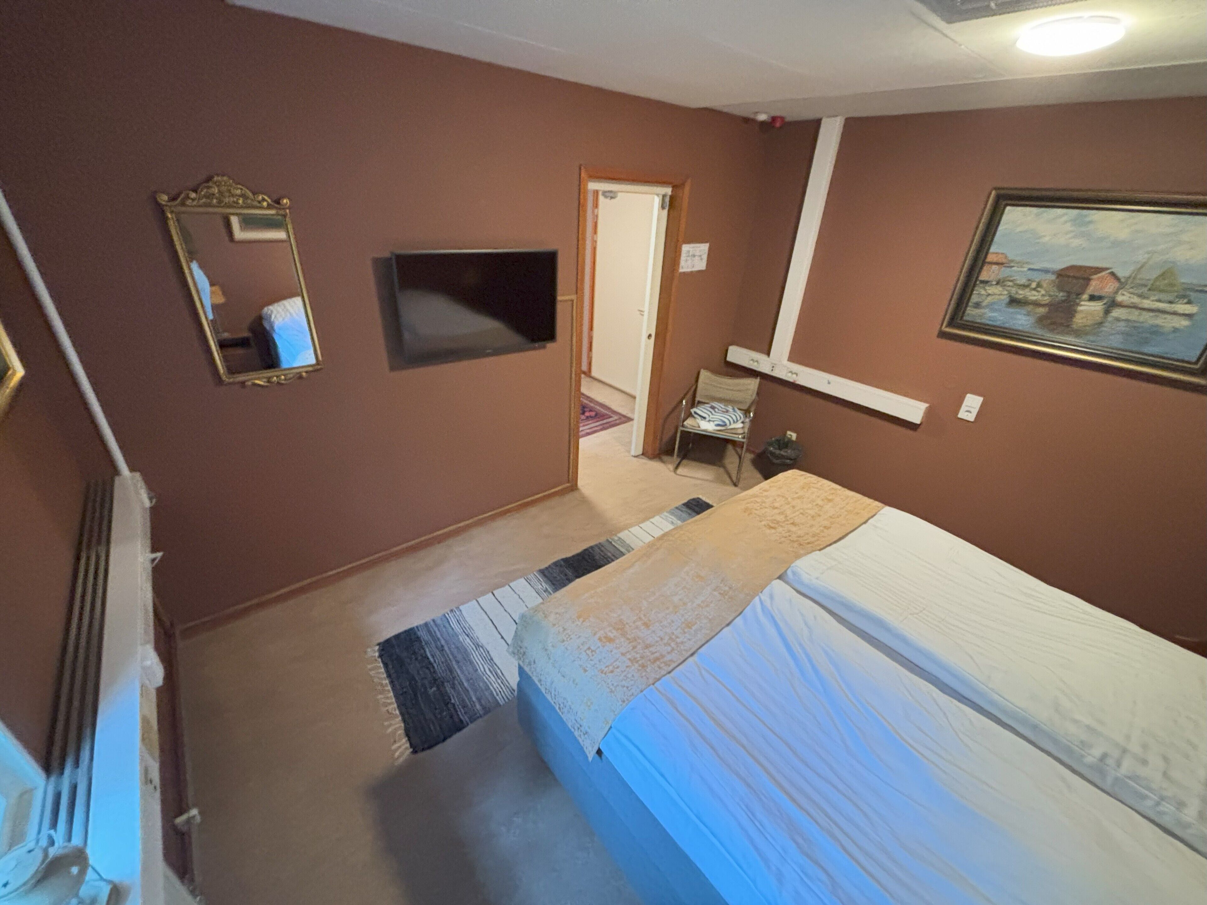 A bedroom with a bed, a television, a chair, and a painting on the wall.