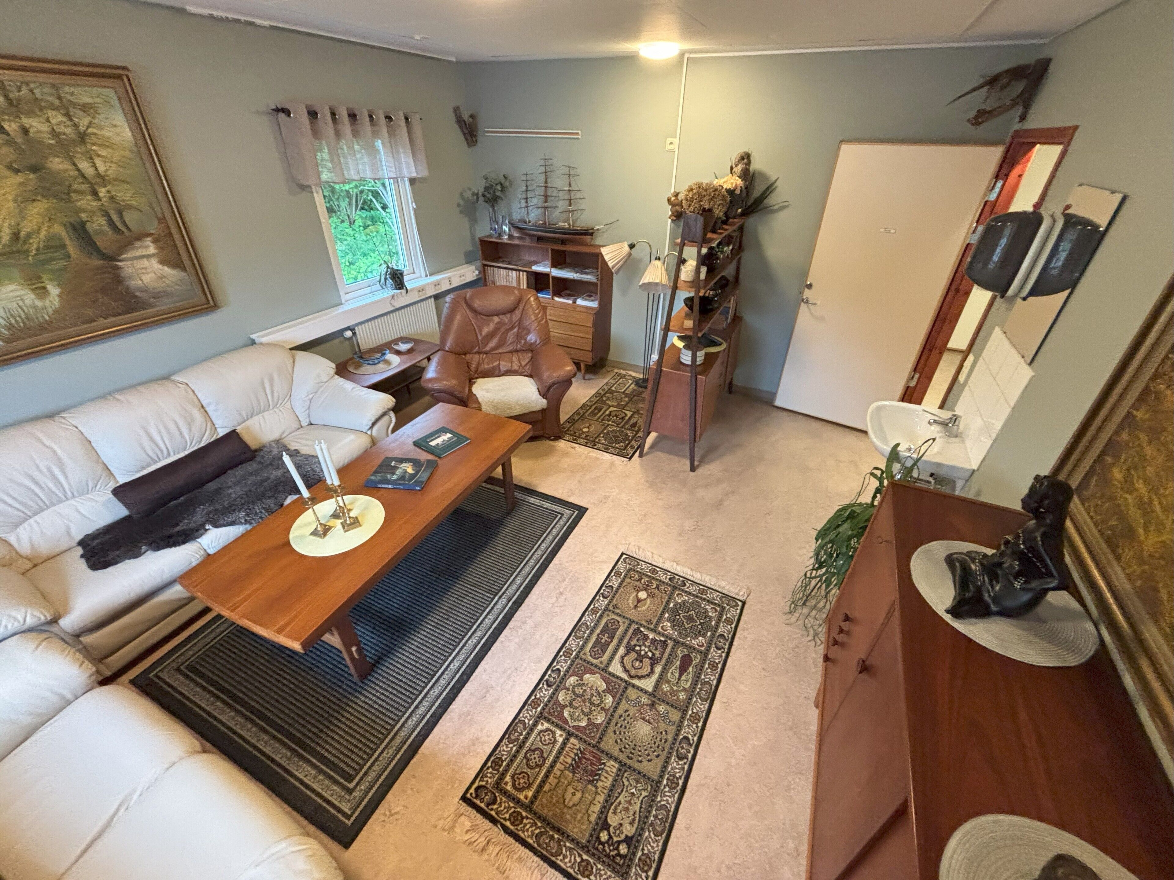 A living room with a sofa, a wooden coffee table, a brown leather chair, a bookshelf, and a small desk.