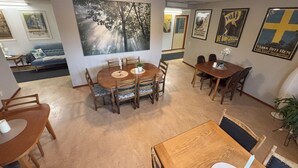 Un comedor con mesas y sillas de madera, un cuadro grande en la pared y varios objetos enmarcados.