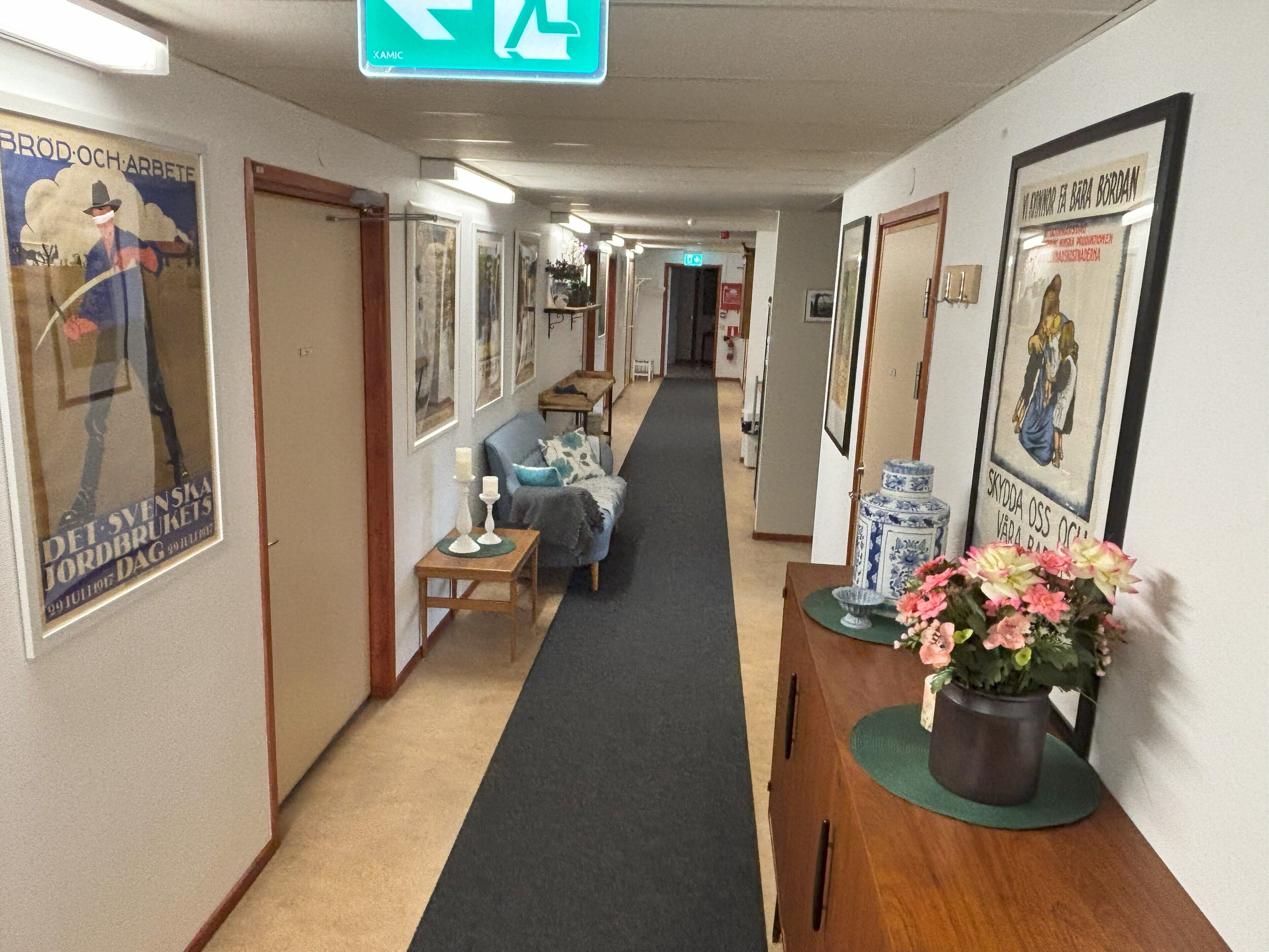 Et hotel med korridor, billeder i rammer, en træreception, en blå sofa og tæppede gulve.