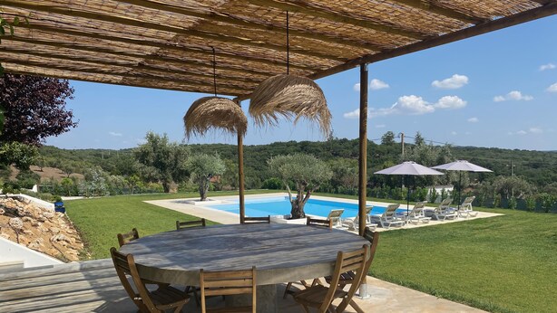 An outdoor patio with a round table and chairs, a pool, and lounge chairs under umbrellas.