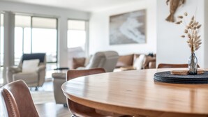 A modern dining area with a round wooden table, cushioned chairs, and a vase with dried flowers. - Bicheno Blue Horizon - The family holiday house! (Glamorgan-Spring Bay)