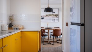 A modern kitchen with yellow cabinets, a dining area with a wooden table and chairs, and a large black pendant light. - Bicheno Blue Horizon - The family holiday house! (Glamorgan-Spring Bay)
