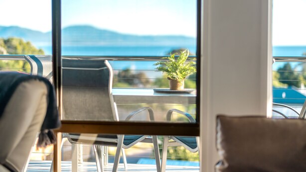 A balcony with chairs and a potted plant, overlooking a scenic view of mountains and a body of water. - Bicheno Blue Horizon - The family holiday house! (Glamorgan-Spring Bay)