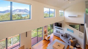 Un vaste espace de vie doté de grandes fenêtres offrant une vue sur les montagnes, d’un téléviseur à écran plat fixé au mur et d’un ventilateur de plafond moderne.