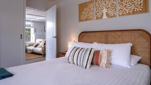 Une chambre avec un grand lit, une tête de lit en rotin et trois œuvres d’art murales.