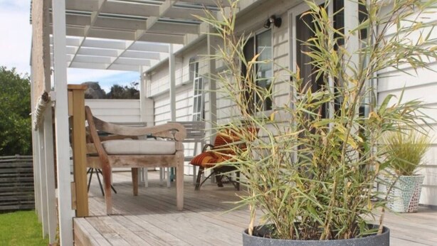 A covered outdoor area with a wooden deck, a large potted plant, and a bench. - Little Champ - True little holiday cabin (Glamorgan-Spring Bay)