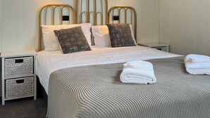 A neatly arranged bedroom with a wooden ceiling, two bedside tables, a bed with a patterned bedspread, and two wall-mounted lights. - Little Champ - True little holiday cabin (Glamorgan-Spring Bay)