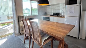 A modern kitchen with a wooden table and chairs, white cabinets, and a built-in microwave. - Little Champ - True little holiday cabin (Glamorgan-Spring Bay)