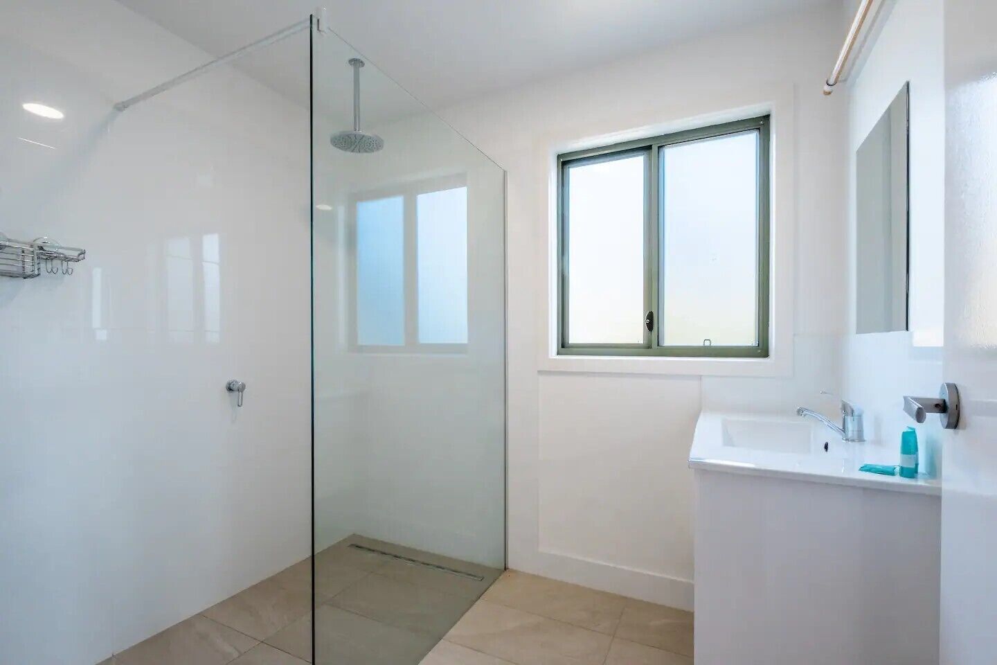A modern bathroom with a glass shower enclosure, a window above the sink, and a white tiled floor.