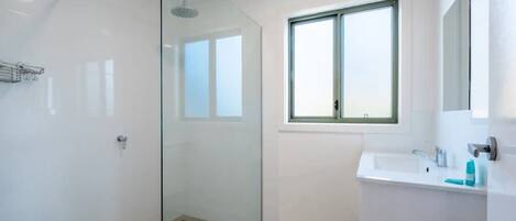 A modern bathroom with a glass shower enclosure, a window above the sink, and a white tiled floor.