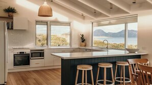 Une cuisine moderne dotée d’un grand îlot central, de tabourets en bois et offrant une vue sur la mer.