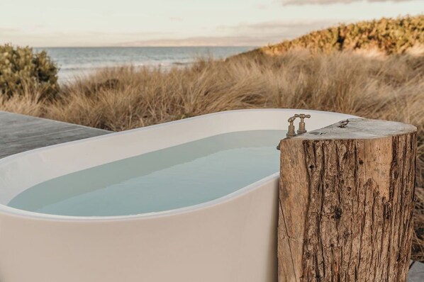 Una vasca da bagno con un supporto in legno, vicino a una spiaggia con erba e vista sull'oceano.