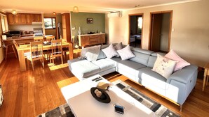 Ein modernes Wohnzimmer mit einer Eckcouch, einem Essbereich mit Holzmöbeln und einer Küche mit Holdekor und Geräten.
