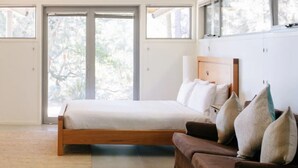 A bedroom with a wooden bed, a brown sofa, and a large window with a view of trees.