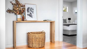 Un salon moderne avec une console en bois, un panier en osier, des plantes séchées et une illustration botanique encadrée.
