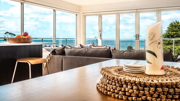 Un salon moderne doté d’une grande fenêtre donnant sur la mer, d’une table à manger en bois et d’un coin salon confortable.
