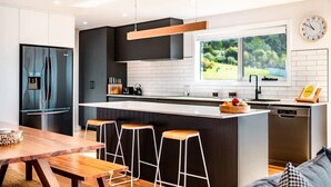 Une cuisine moderne dotée d’un îlot central, de meubles noirs et d’une fenêtre donnant sur un espace verdoyant.