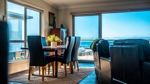 A modern living room with a dining area, large windows, a view of the ocean, and a balcony. - Ocean Sunrise - Beautiful views! (Glamorgan-Spring Bay)