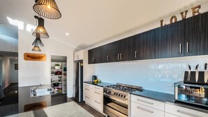 A modern kitchen with dark wooden cabinets, a stainless steel stove, and a built-in oven. There is a countertop with a sink and a knife block. - Ocean Sunrise - Beautiful views! (Glamorgan-Spring Bay)