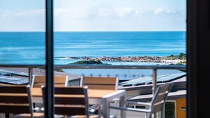 A view from a balcony overlooking the ocean with a rocky shoreline and solar panels on the buildings. - Ocean Sunrise - Beautiful views! (Glamorgan-Spring Bay)