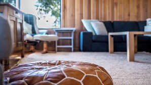 Una sala acogedora con un reposapiés de cuero, un sofá oscuro y una mesa de centro de madera.