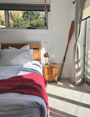 Un dormitorio con cama, mesita de noche, una paleta de madera y ventana con vista a árboles.