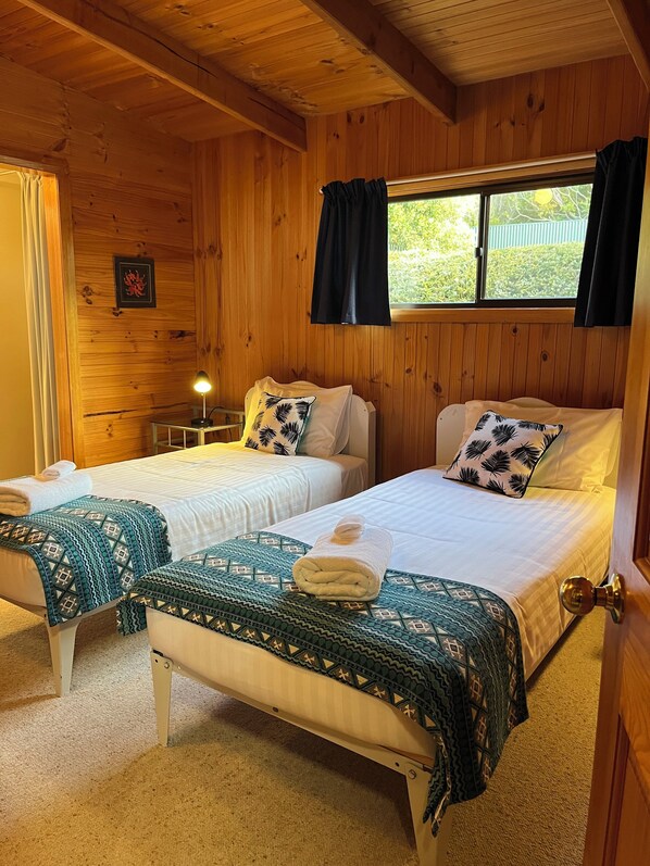 Una habitación de cabaña de madera con dos camas, cada una con colcha y almohadas estampadas, una mesita con lámpara y una ventana con cortinas.