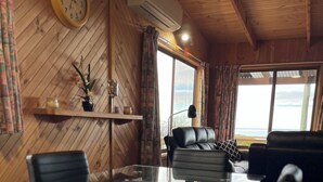 Un interior de madera con una mesa de vidrio, sillas de cuero, un sofá, un reloj y vistas al mar.