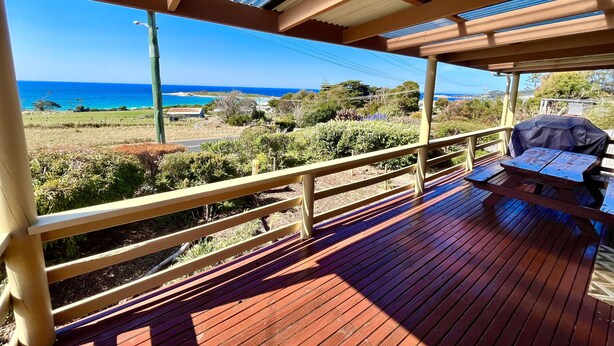 Una terraza de madera con techo, con vistas a un paisaje costero que incluye el océano y colinas al distante.