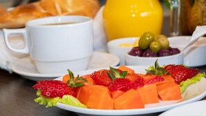 A breakfast setting with a plate of fruit, a cup of coffee, a jug of orange juice, and a loaf of bread. - Alsacia Boutique Hotel (Arequipa)
