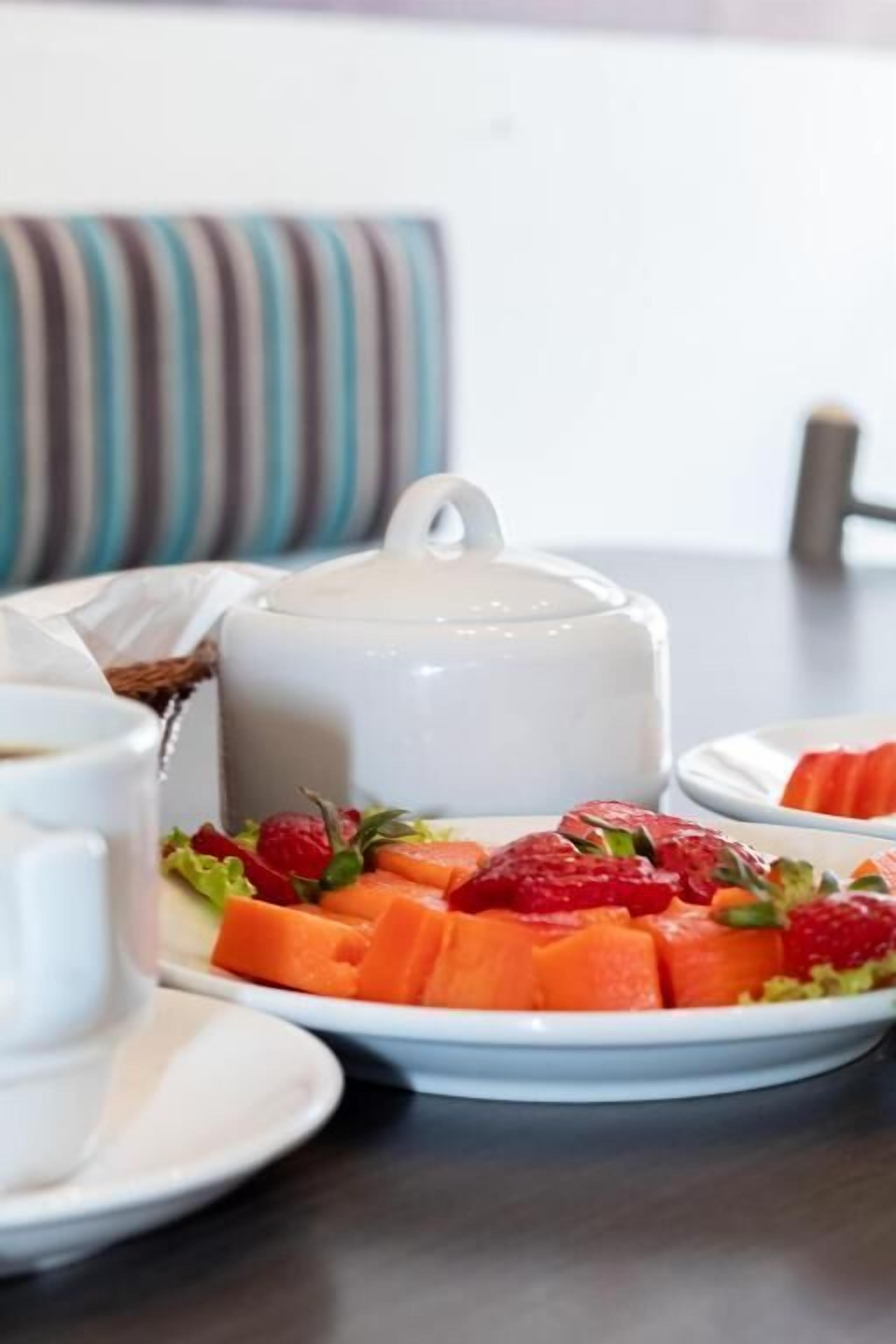 A table with a white teapot, a plate of sliced fruits, and a cup.